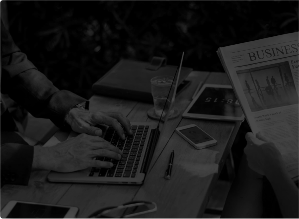 Black and white photo of people working outdoors with a laptop and a business newspaper